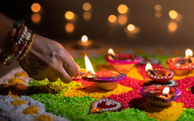 Hand adorned with bangles lighting a diya