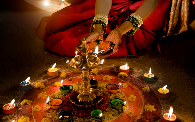 Woman lighting diyas decorated by colourful rangoli