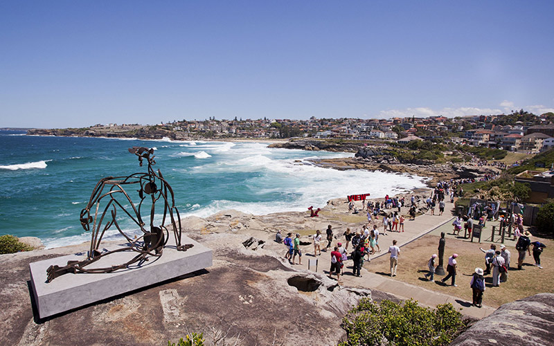 Metal sculpture overlooking the ocean along the Bondi to Coogee coastal walk, with waves and people walking along the shoreline.