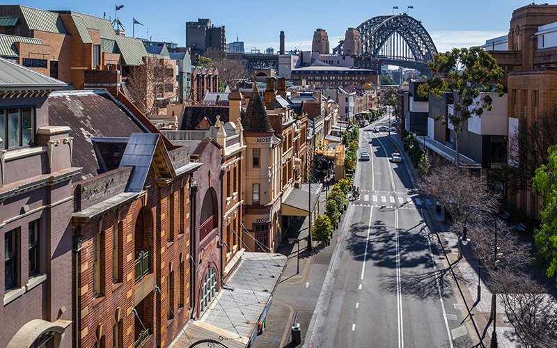 Historic buildings along a street in The Rocks with the Sydney Harbour Bridge visible in the background.