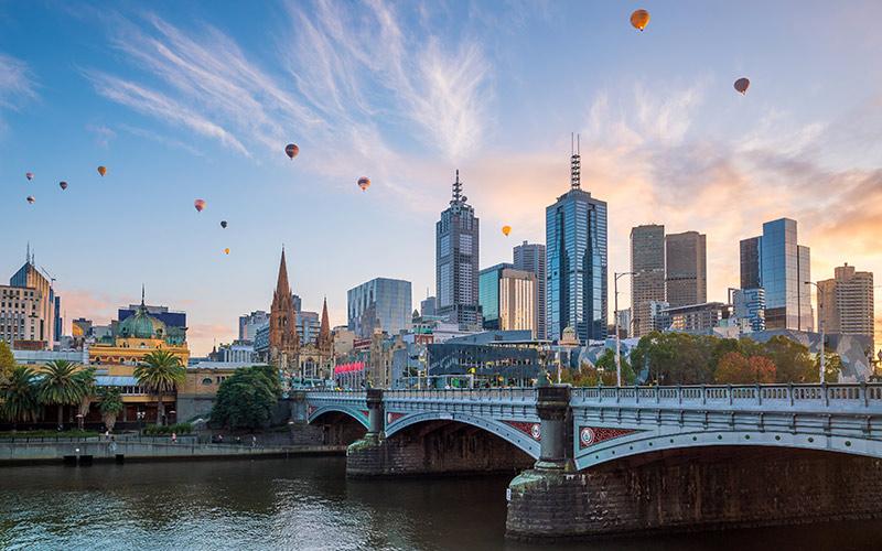Melbourne city skyline at sunrise with hot air balloons floating above buildings and a bridge over the Yarra River