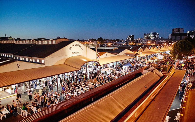 Busy evening crowd at Queen Victoria Market with lit stalls and people dining and walking through the market